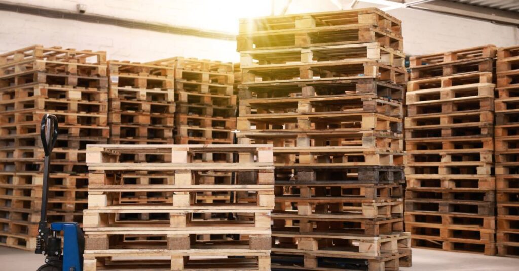 Multiple stacks of pallets outdoors. There's a mix of both wooden and blue and black plastic pallets strewn about.