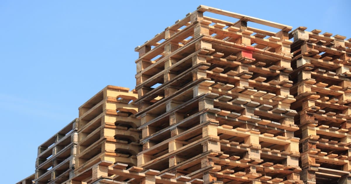 An angled view of several stacked wooden pallets. The stacks in front have a different construction than the ones in back.