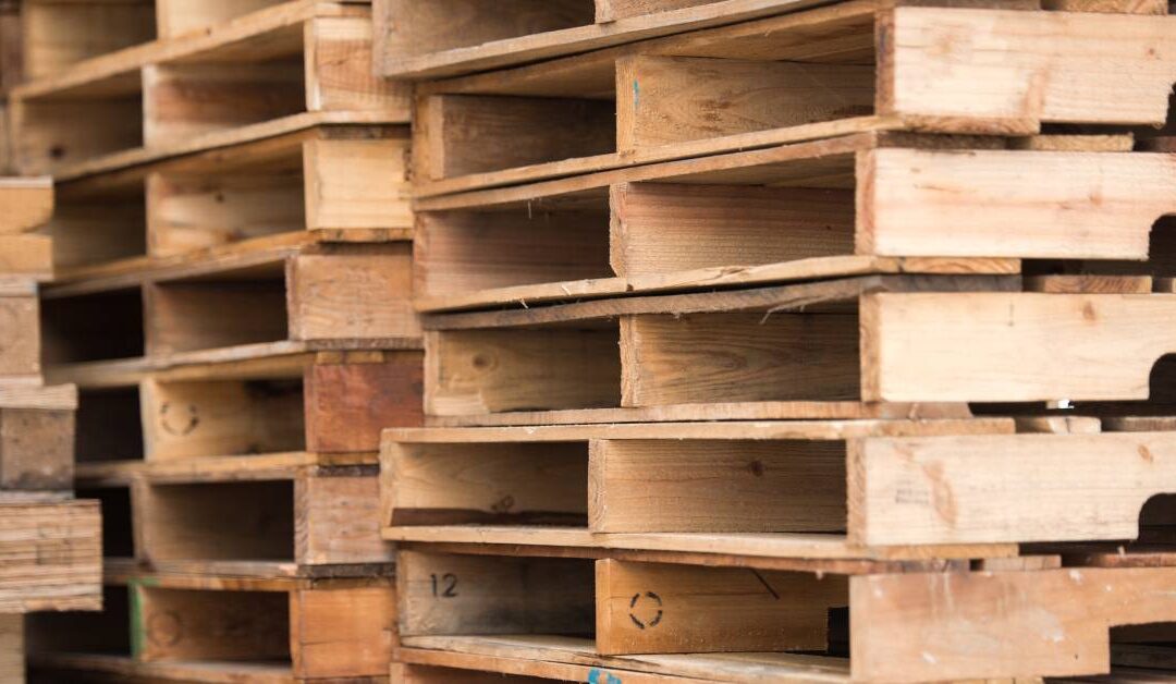 Three tall stacks of wooden pallets feature various stamps of a segmented circle on the inside of the boards.