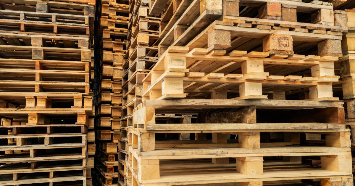 Multiple towering stacks of used wooden cargo pallets sit next to each other inside a warehouse facility.