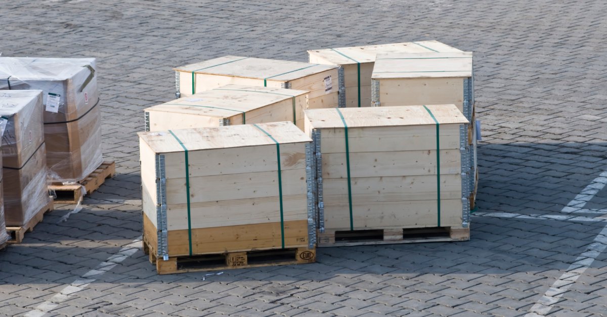 Several small wooden pallets on a brick ground. They have wooden crates on top with protective metal plates on the corners.