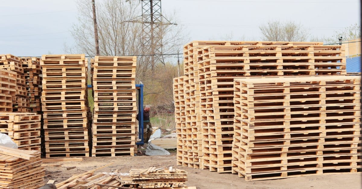 Several large stacks of industrial-sized wooden pallets neatly lined up in an outdoor logistics area.