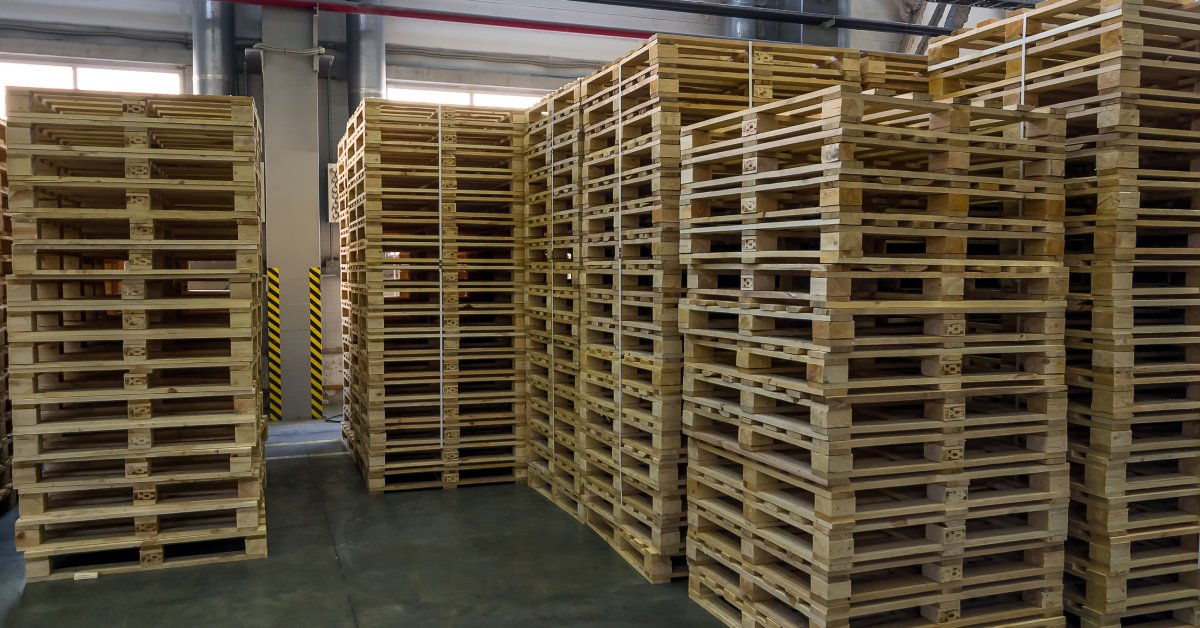 Multiple stacks of wooden pallets inside a designated loading zone in a warehouse. One stack is shorter than the others.