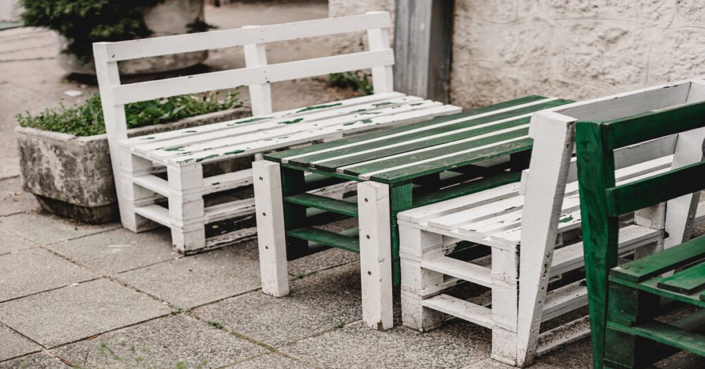 A pair of wooden benches and a table sitting on a concrete floor. The furniture is made out of recycled wooden pallets.