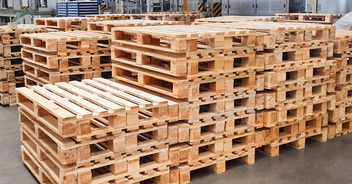 Several stacks of wooden pallets lined up next to one another in a warehouse. The stack in the front is slightly shorter.