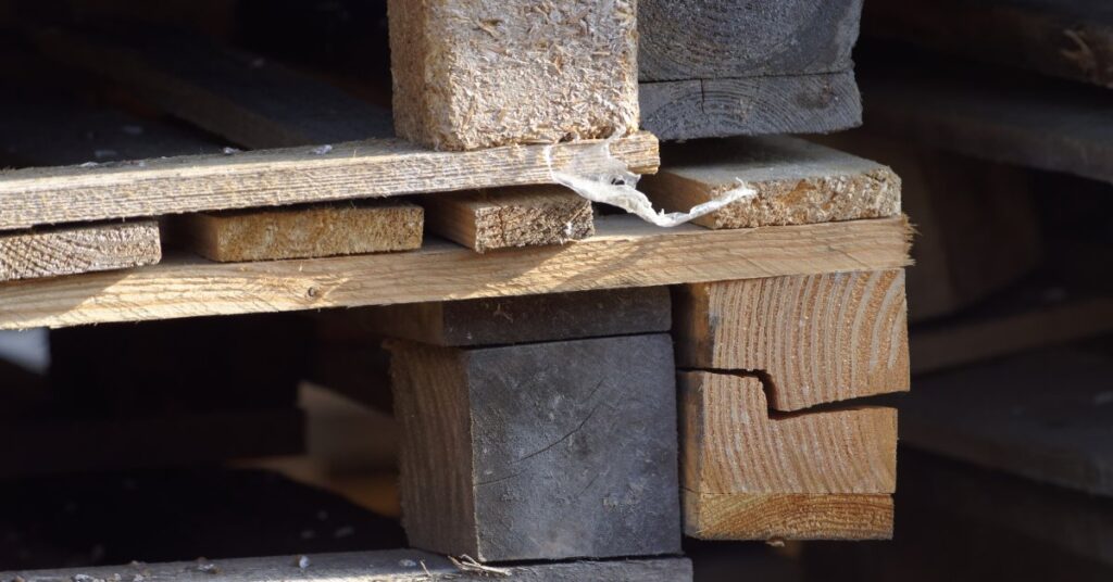 A close-up view on two wooden pallets stacked together. The corners and fasteners are cracked and damaged.
