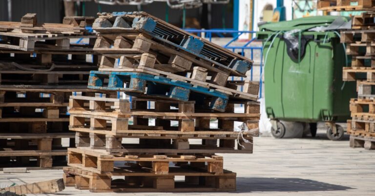 A tall stack of improperly balanced wooden pallets set up outside. The tower is top-heavy and leaning off to the right.