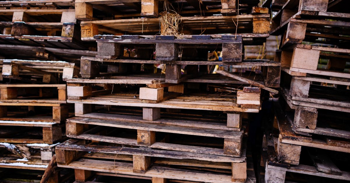 Three tall stacks of wooden pallets. The wood is wet and worn down in many places, showcasing visible damage.