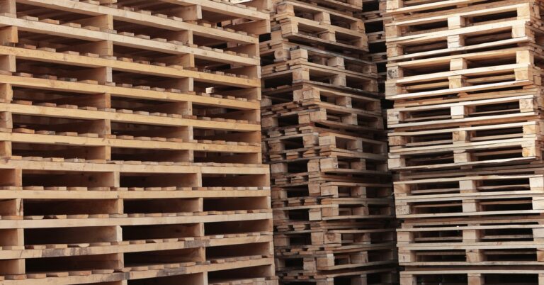 Dozens of wooden pallets that are not currently in use are collected together in tall stacks in a corner.