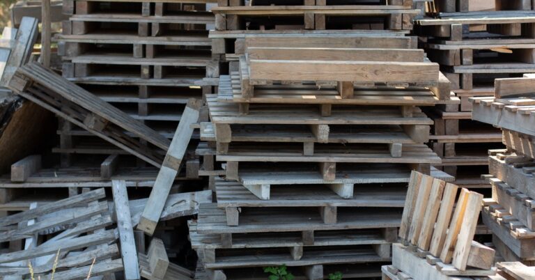Wooden pallets sorted in multiple stacks with some broken into multiple pieces and scattered into piles.
