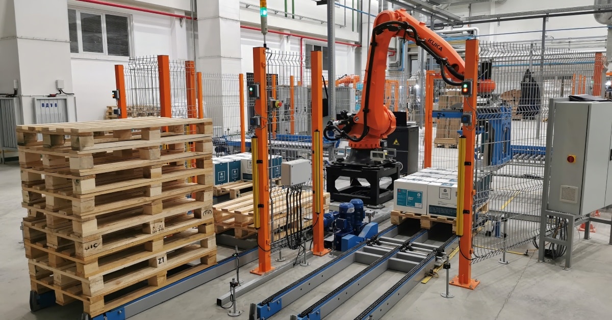 A facility with an automated orange robotic arm and stacks of wooden pallets on various rails for movement.