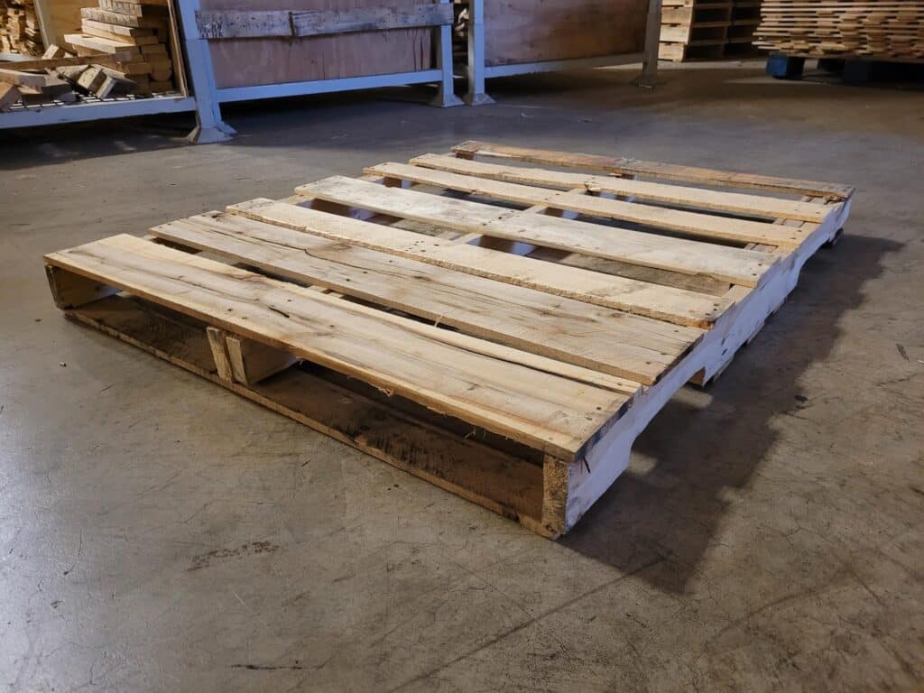 Economical Grade B recycled wooden pallet showing stringer plug repairs resting on a concrete warehouse floor in Milwaukee.